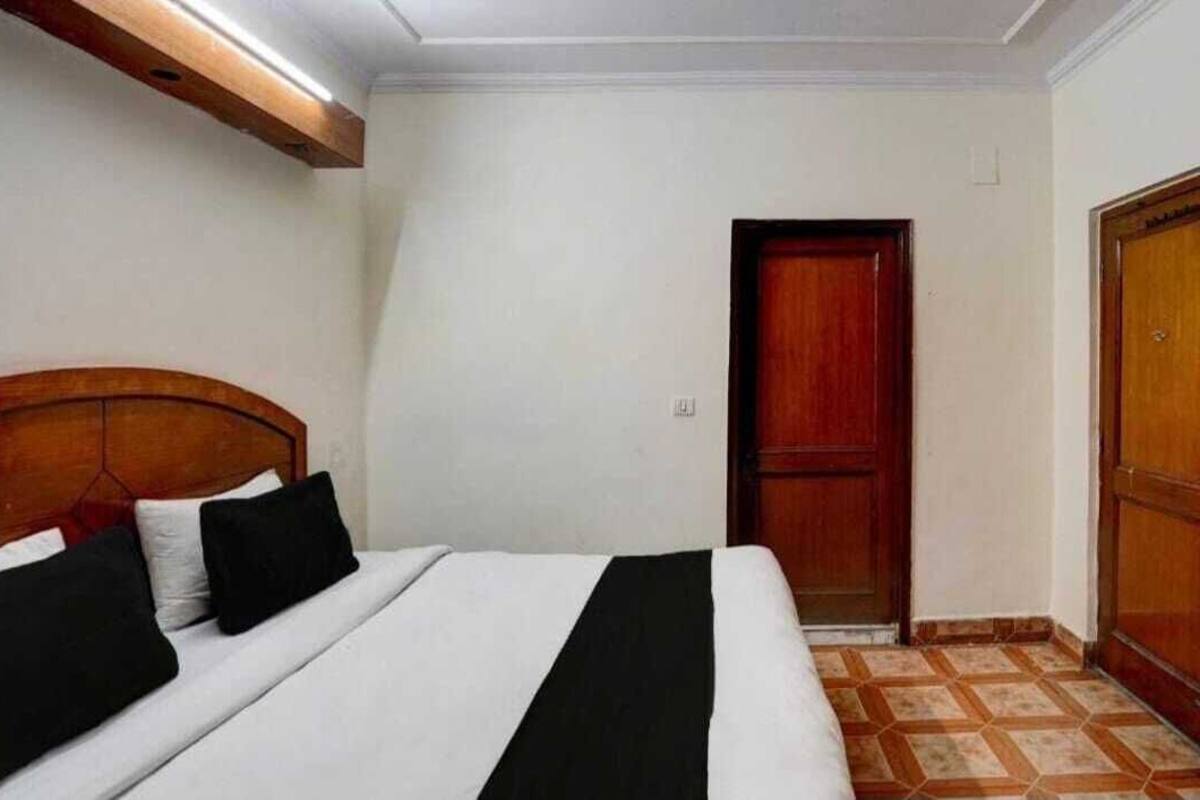 A hotel room with a bed, a wooden headboard, a red door, and a tiled floor.