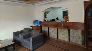 Un área de recepción con un mostrador de madera, una zona de estar con dos sillones grises y un candelabro en el techo.