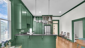 Una cocina con gabinetes verdes, una isla central, electrodomésticos de acero inoxidable e iluminación colgante.