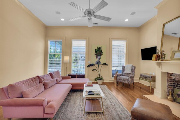 A living room with a pink sofa, a coffee table, a fireplace, and a ceiling fan.