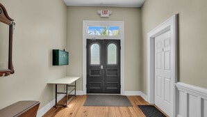 Un pasillo con suelo de madera, un banco, una puerta con paneles de vidrio esmerilado y un letrero de salida encima de la puerta.