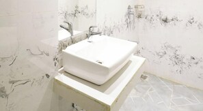 A bathroom with a white sink, a mirror, and a marble wall. - Hotel Gorrion (Mumbai)