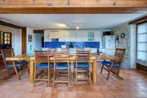A kitchen with a wooden table and chairs, white cabinets, and a stone wall.