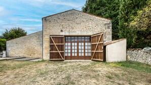 A stone building with a large wooden door and windows, surrounded by grass and trees. - Holiday Home 'La Musardière' with Private Pool, Private Terrace and Wi-Fi (Champagnolles)