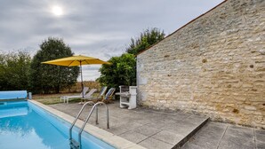 A swimming pool with a stone wall, lounge chairs, and an umbrella. - Holiday Home 'La Musardière' with Private Pool, Private Terrace and Wi-Fi (Champagnolles)