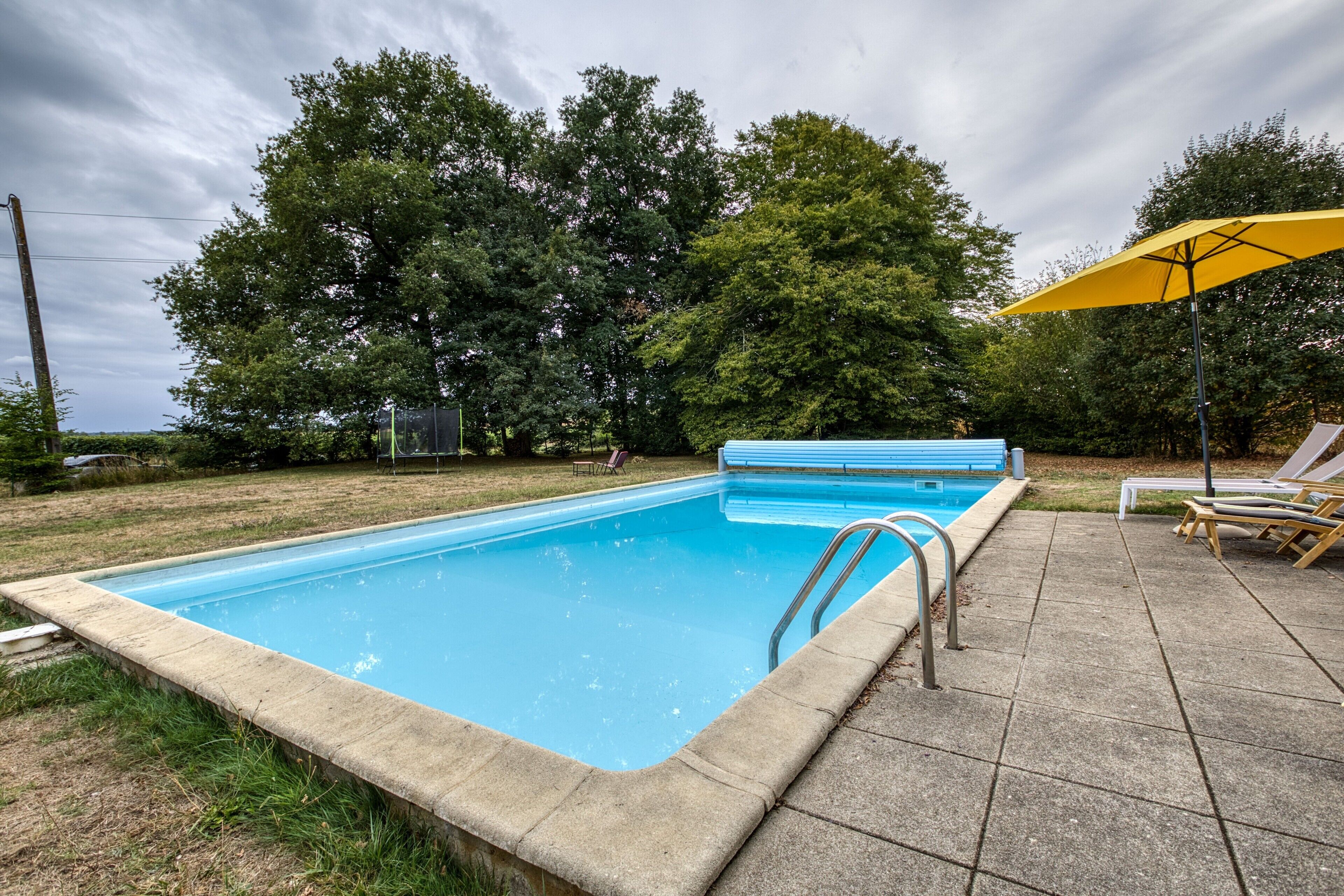 A rectangular swimming pool with a metal ladder, surrounded by a concrete deck.