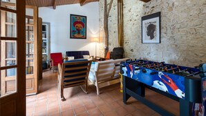 A room with a foosball table, a bed, a red chair, and a wooden door. - Holiday Home 'La Musardière' with Private Pool, Private Terrace and Wi-Fi (Champagnolles)
