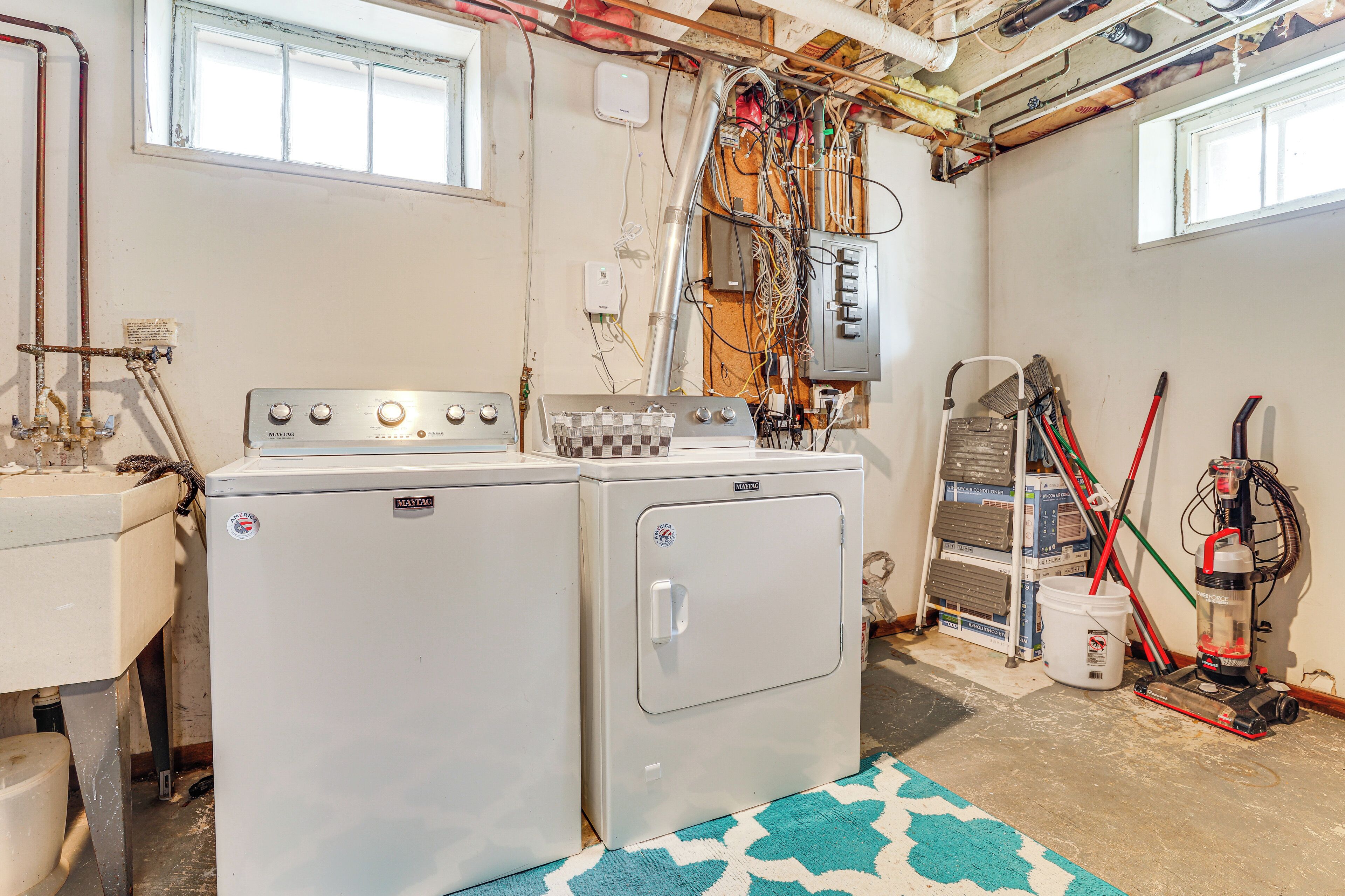 Une buanderie équipée de deux machines à laver Maytag, d’une fenêtre et de divers outils de nettoyage.