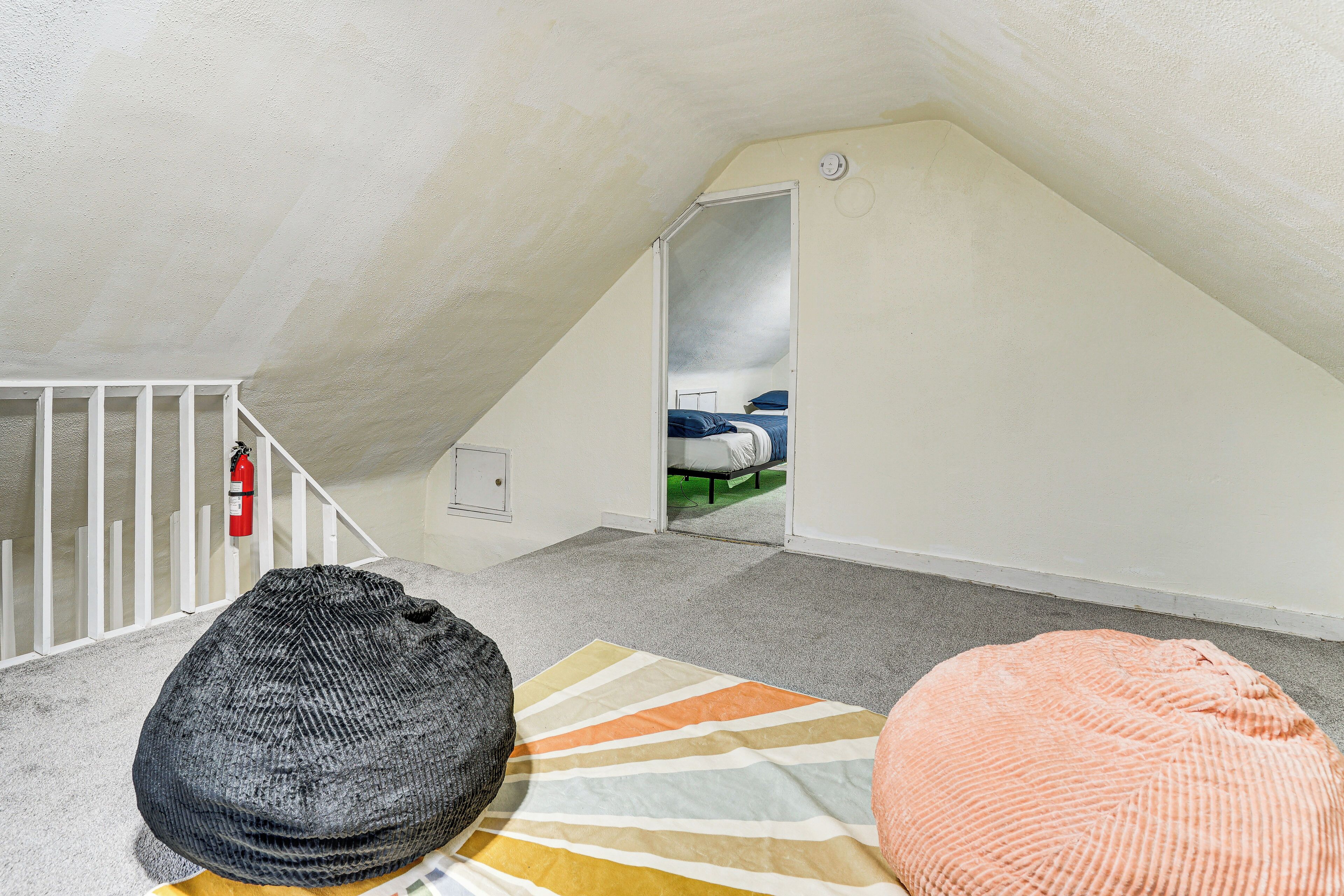 A room with a sloped ceiling, a fire extinguisher, a bed with a blue and white mattress, and two bean bags.