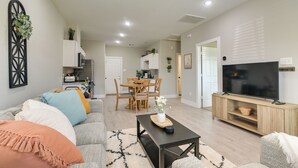 Ein modernes Wohnzimmer mit Sofa, Couchtisch und Fernseher. Im Hintergrund ist ein Essbereich mit Tisch und Stühlen zu sehen.