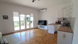 A spacious living room with a wooden floor, a sofa, a television, and a kitchen area with cabinets and a countertop. - MyDream apartment No.2 (Dramalj)
