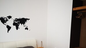 A bedroom with a bed, pillows, a world map wall decoration, a wooden shelf, and a hanging rack. - MyDream apartment No.2 (Dramalj)