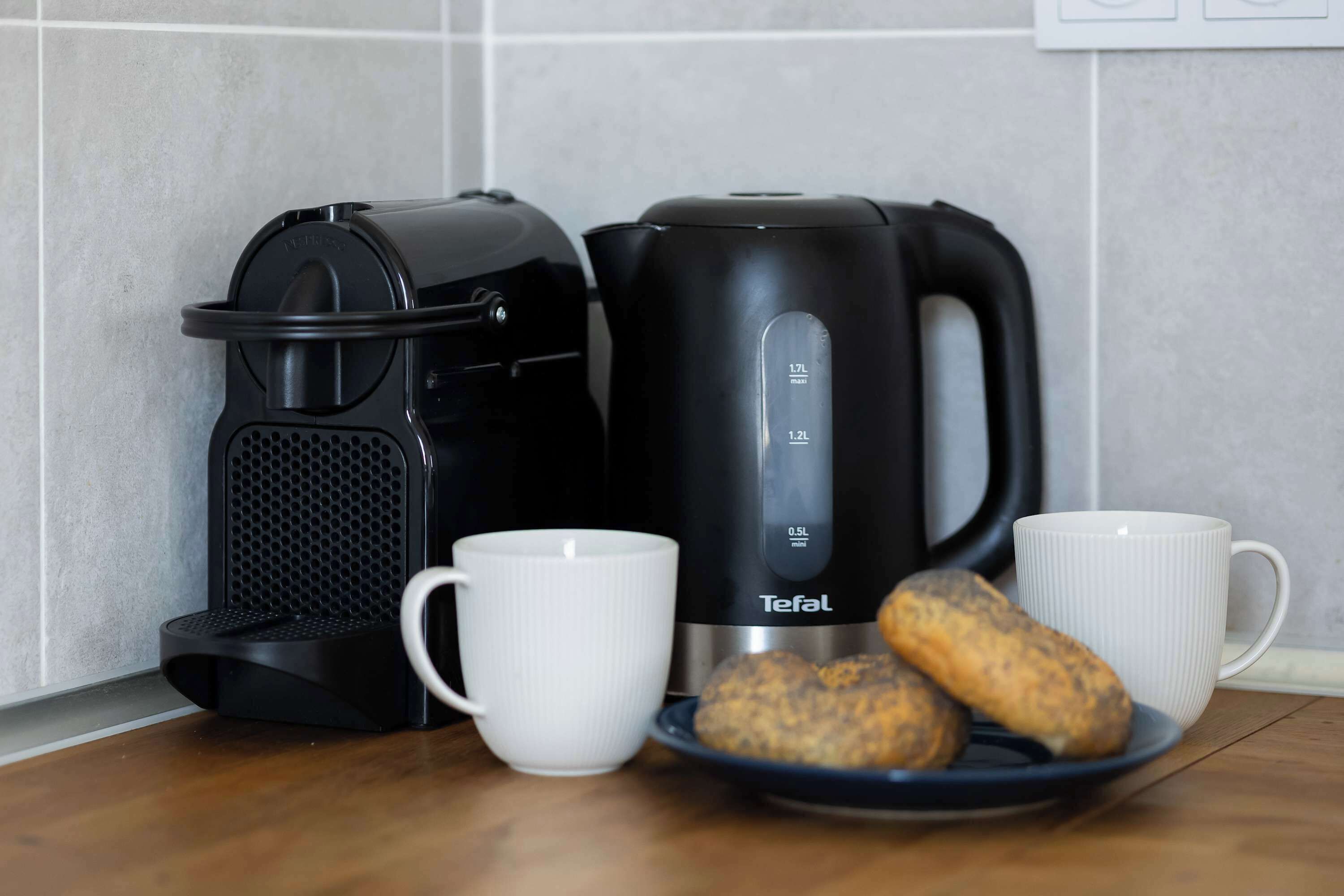 Eine Küche mit Kaffeemaschine, Wasserkocher und zwei weißen Tassen auf einem Holztisch.