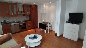 A modern living room with a sofa, a coffee table, a dining table with chairs, a kitchen area with cabinets and appliances, and a TV. - Central Narvik Apartment, Walk to Train & Bus (Narvik)
