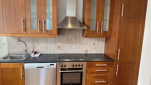 A kitchen with wooden cabinets, a stainless steel range hood, a dishwasher, an oven, and a black countertop. - Central Narvik Apartment, Walk to Train & Bus (Narvik)