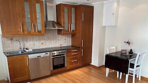 A compact kitchen with wooden cabinets, a built-in oven, and a black countertop. - Central Narvik Apartment, Walk to Train & Bus (Narvik)