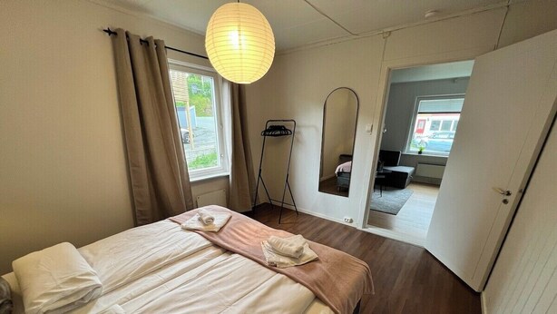 Un lit bien fait, avec du linge de lit blanc et beige, une lampe sur pied et un miroir au mur.