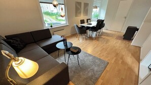 Un salon moderne avec un canapé d’angle, une petite table ronde et un coin repas avec des chaises.