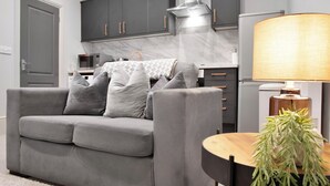 Ein modernes Wohnzimmer mit einem grauen Sofa, einem runden Holztisch und einer Topfpflanze.