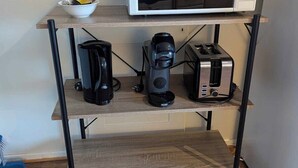 Une petite cuisine équipée d’un four à micro-ondes posé sur une étagère, d’une machine à café et d’un grille-pain.