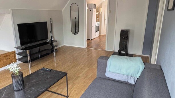 Un salon moderne avec un canapé gris, un meuble TV noir et un plancher en bois.