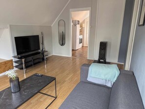 A modern living room with a grey sofa, a black TV stand, and a wooden floor. - Railway loft apartment (OJ1-3) (Narvik)