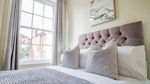 A bedroom with a large window, a tufted headboard, and a view of buildings outside. - WhiskAwayHomes Shaw Street Apartment 5 (Worcestershire)