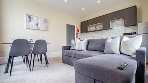 A modern living room with a grey sofa, a dining table with chairs, and a kitchen area with dark cabinets and a marble backsplash. - WhiskAwayHomes Shaw Street Apartment 5 (Worcestershire)