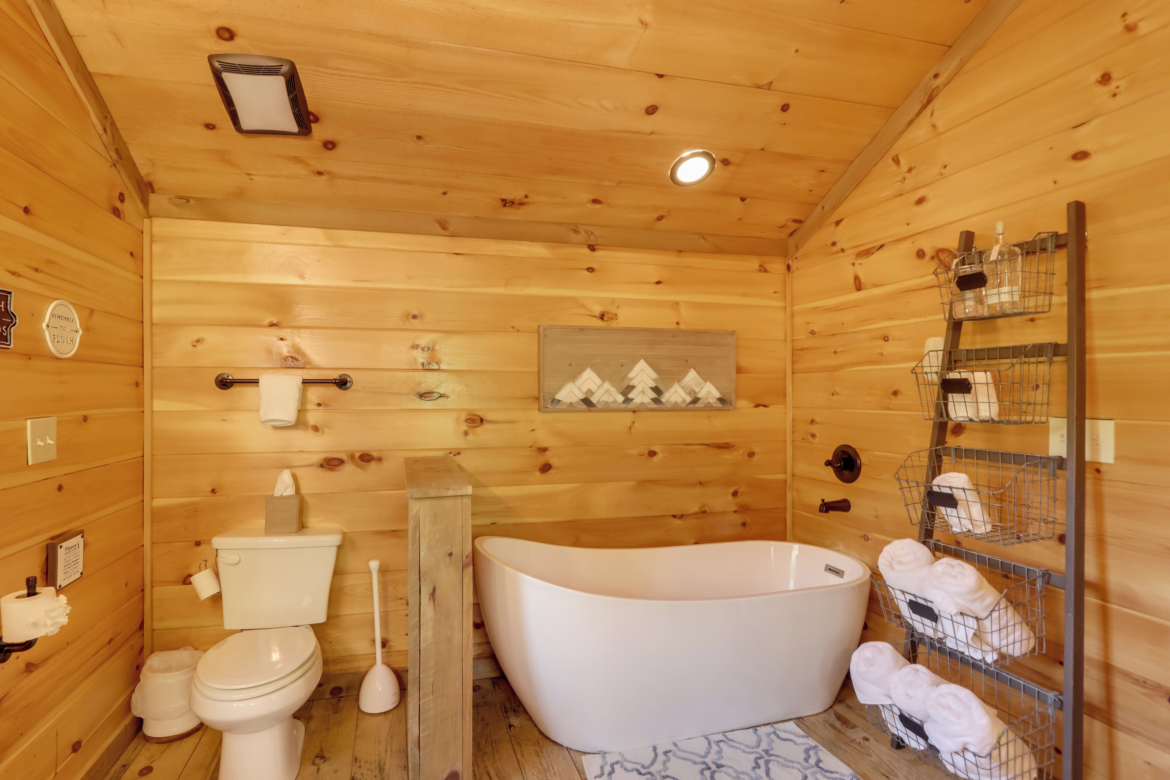 A wooden cabin bathroom with a toilet, sink, and freestanding bathtub.