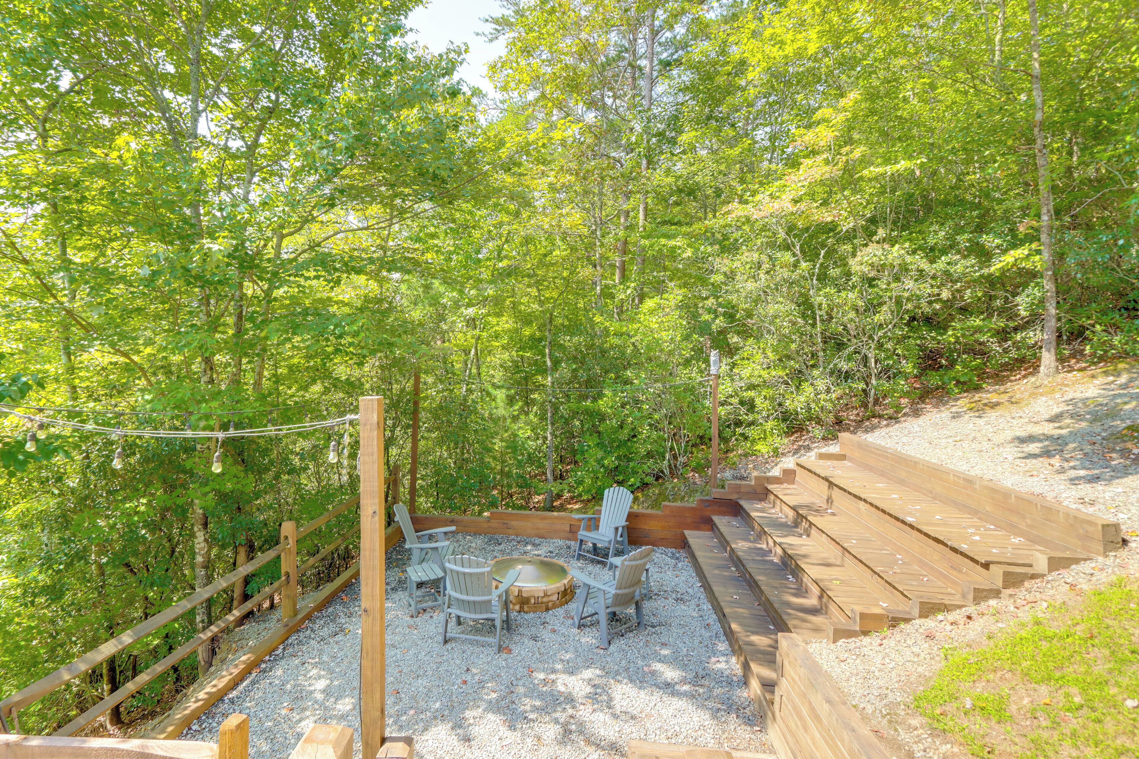 Une terrasse en bois avec des sièges d’extérieur et un foyer, le tout entouré de gravier, situé dans une zone boisée.