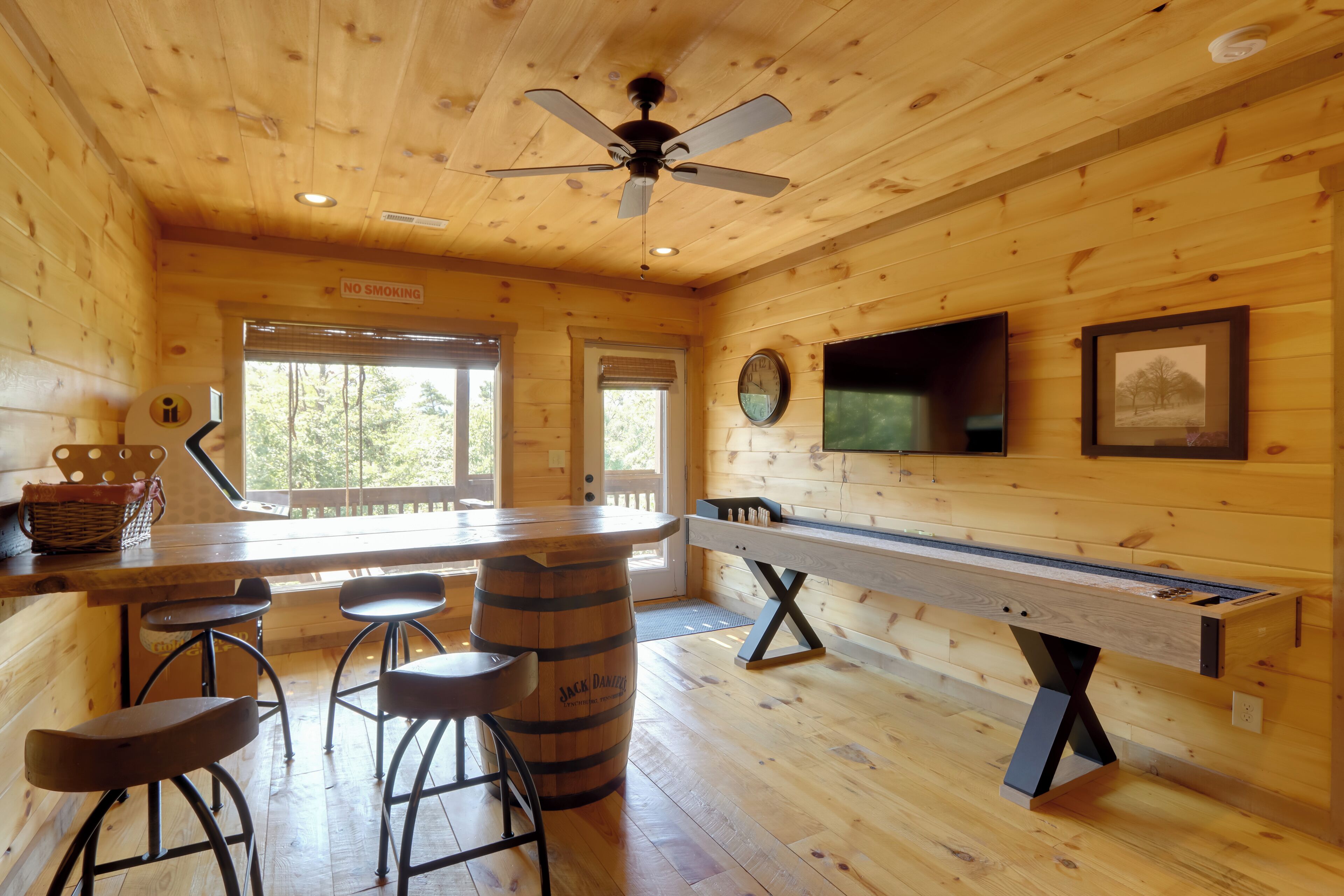 A wooden cabin interior with a bar area, stools, a pool table, and a ceiling fan.