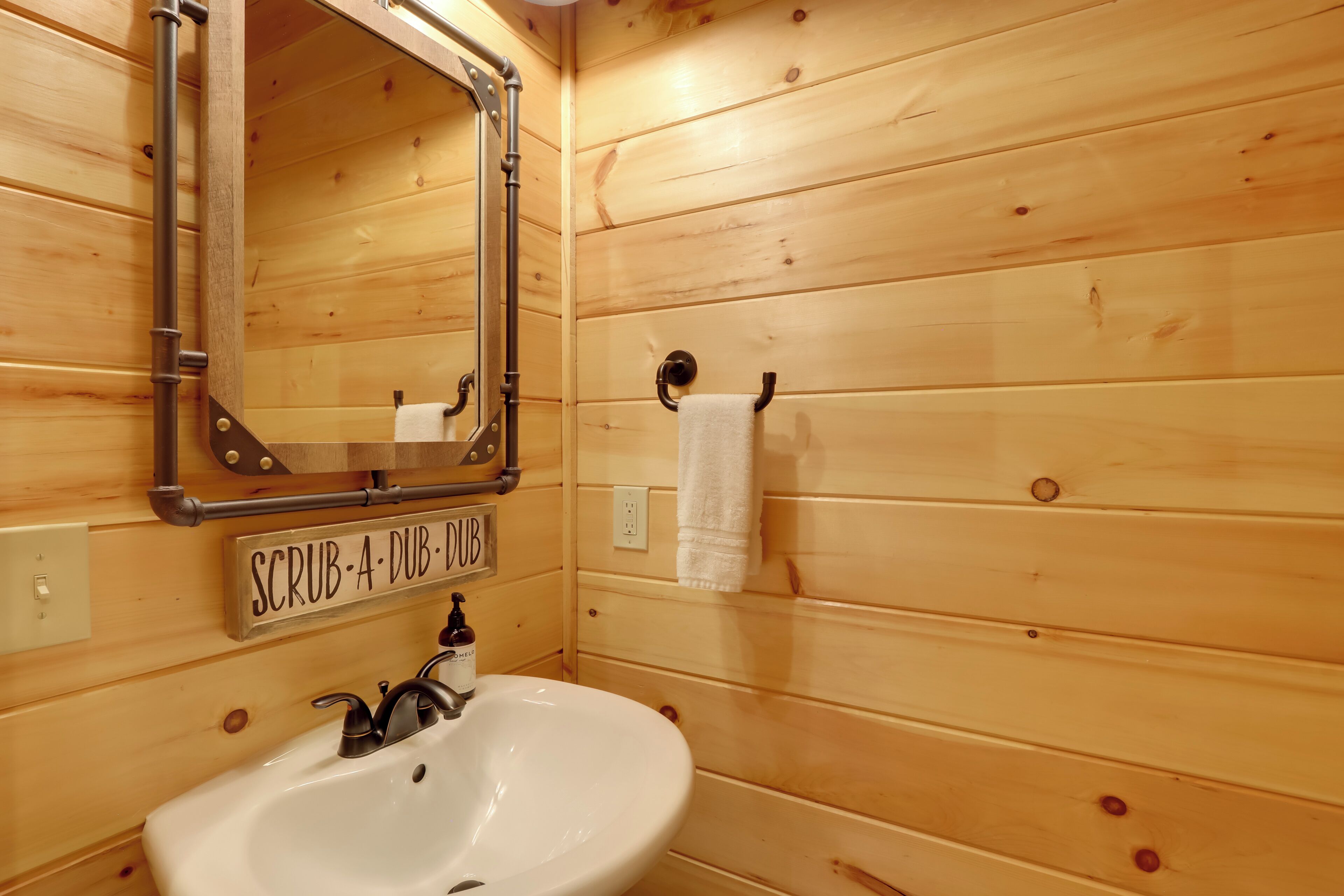 A wooden cabin bathroom with a white sink, a mirror, and a towel hanging on a rack.