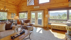 Interior acogedor de una cabaña de madera con una ventana grande, un sofá, una silla y una mesa de comedor.