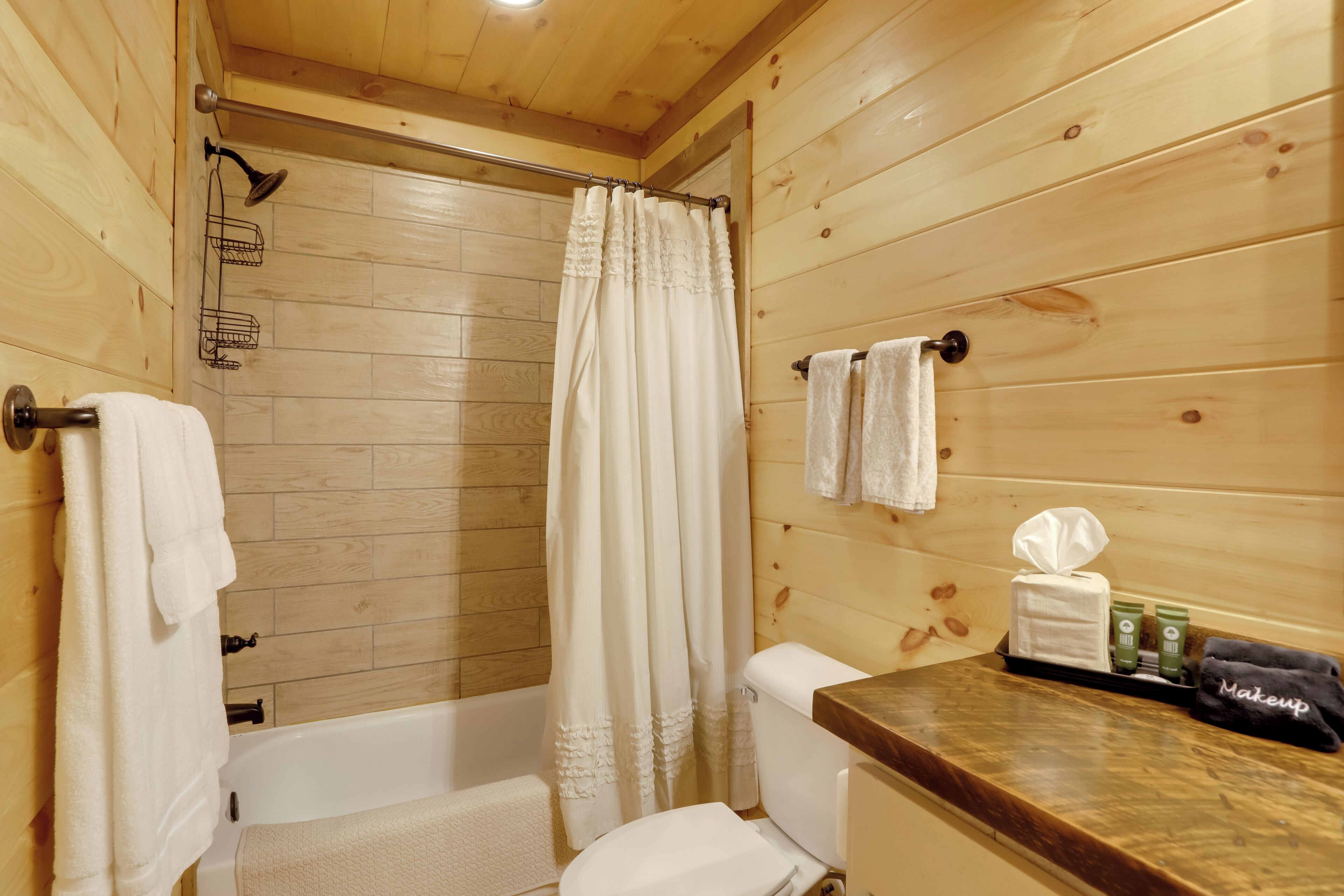 Une salle de bain en bois équipée d’une douche, de toilettes et d’un meuble-lavabo avec des articles de toilette.