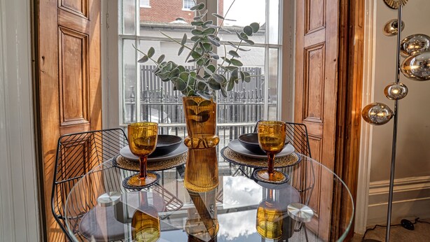 A dining table with a glass top, surrounded by chairs, a vase with a plant, and a floor lamp.
