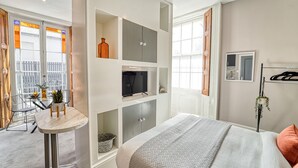 A modern bedroom with a bed, built-in shelving, a small table, and a TV.