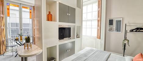 A modern bedroom with a bed, built-in shelving, a small table, and a TV.