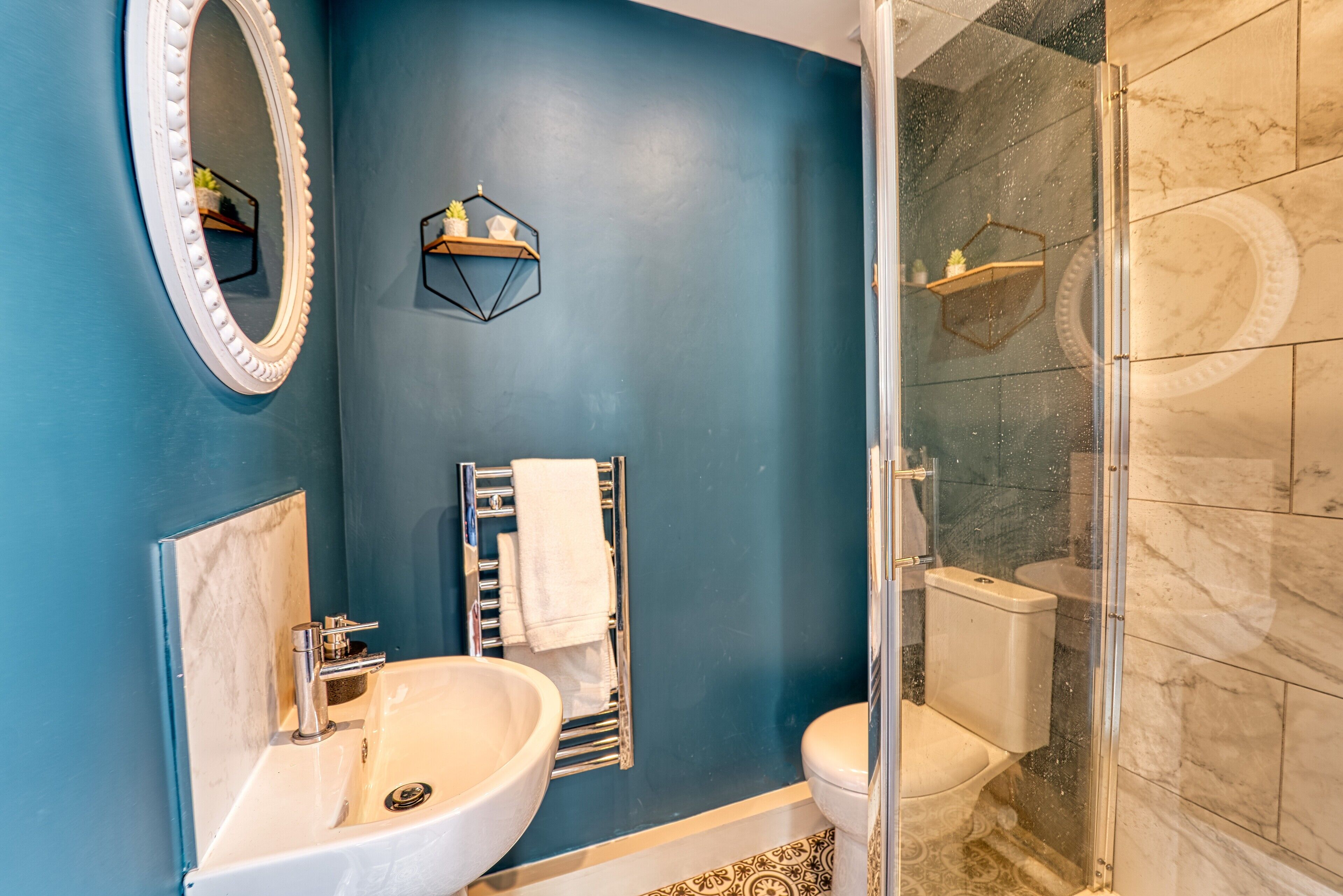 A bathroom with a blue wall, a white sink, a mirror, a toilet, and a glass shower enclosure.