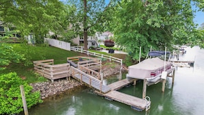 A dock with a boat, a wooden bridge, and a grassy area with trees.