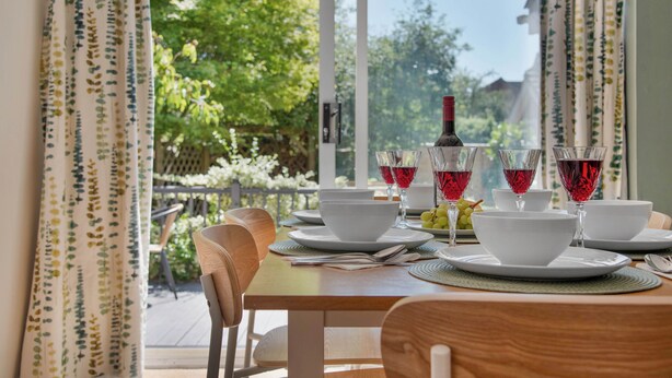 A dining table set with white bowls, plates, and cutlery, with red wine glasses and a bottle on the table. - WhiskAwayHomes Pirie Avenue No. 2 (Worcestershire)
