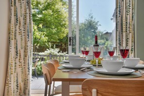 A dining table set with white bowls, plates, and cutlery, with red wine glasses and a bottle on the table. - WhiskAwayStays Pirie Avenue No. 2 (Worcestershire)