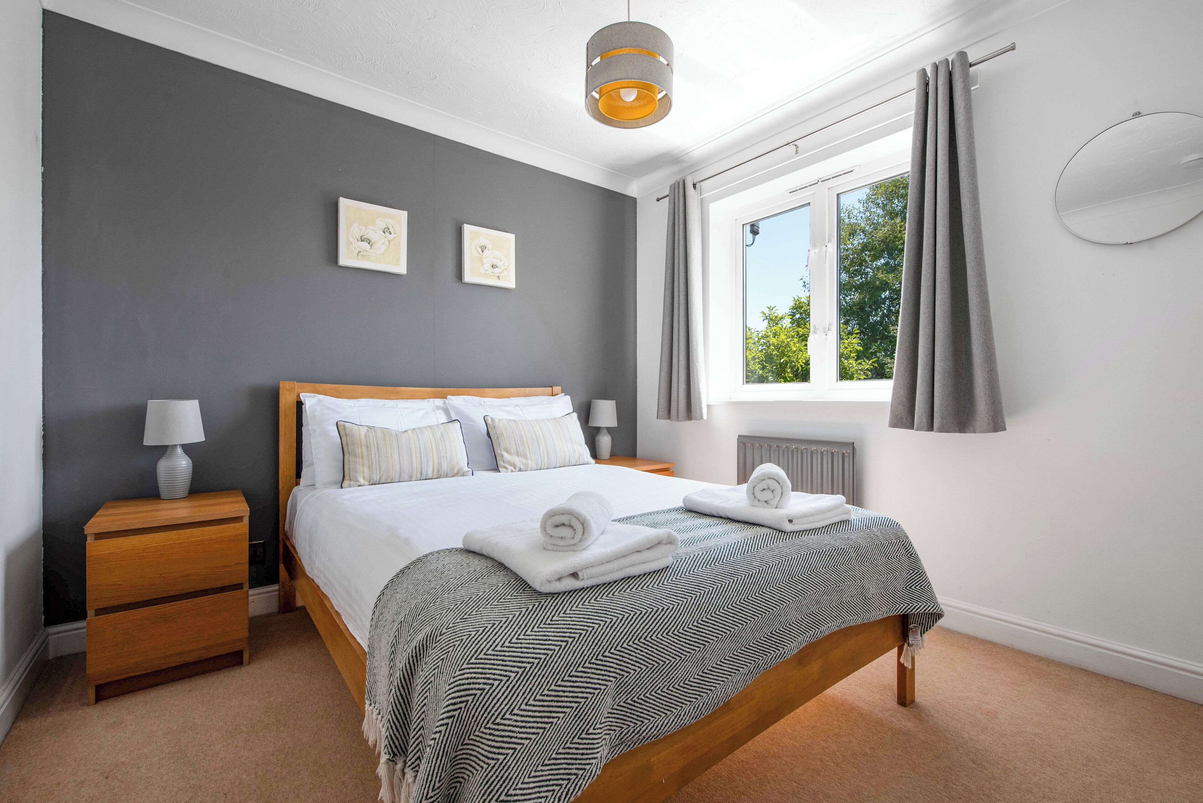 A bedroom with a large bed, a nightstand, a lamp, and a window with curtains.