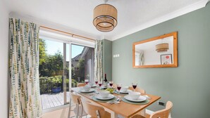 A dining area with a table set for four, a mirror on the wall, and a view of a garden through the window. - WhiskAwayHomes Pirie Avenue No. 2 (Worcestershire)