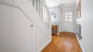 A hallway with white walls, wooden flooring, a white staircase, and a door with diamond-patterned glass. - WhiskAwayHomes Pirie Avenue No. 2 (Worcestershire)