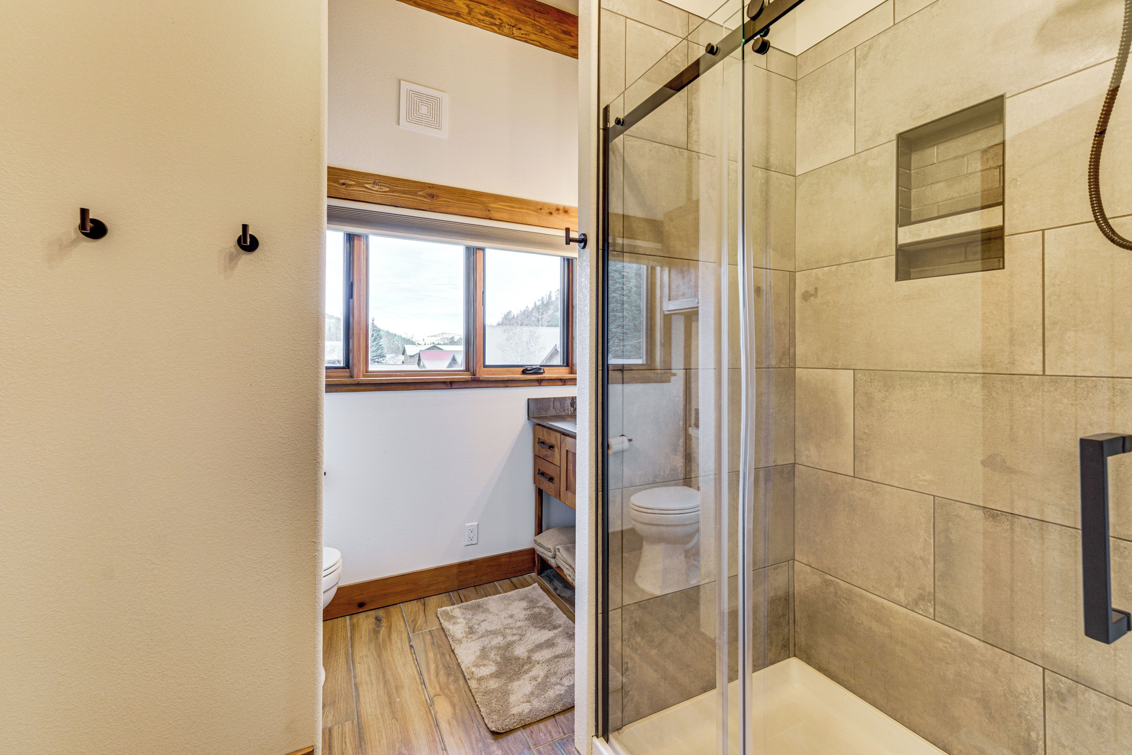 Ein Badezimmer mit einer gläsernen Duschkabine, einer Toilette und einem Fenster mit Blick ins Freie.