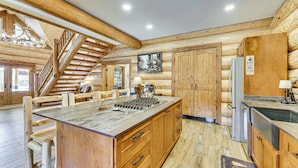 Interior de una cabaña de troncos con una isla central, una escalera de madera y una zona de cocina con electrodomésticos.