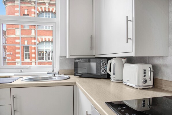 A modern kitchen with a window, a sink, a microwave, a kettle, and a toaster. - WhiskAwayStays Taylor Bennett Apartment 3 (Worcestershire)