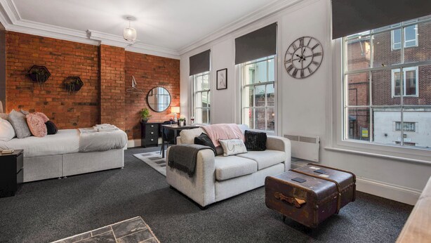Een moderne woonkamer met een bakstenen muur, twee banken, een salontafel en een groot raam.