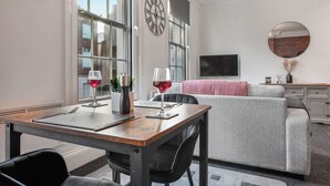 Een moderne woonkamer met een eettafel, twee stoelen, een grijze bank en een groot raam.