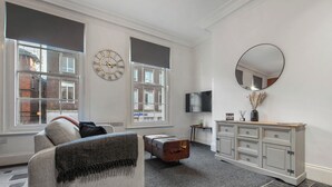 Een moderne woonkamer met een bank, een vintage koffer, een televisie en een spiegel aan de muur.